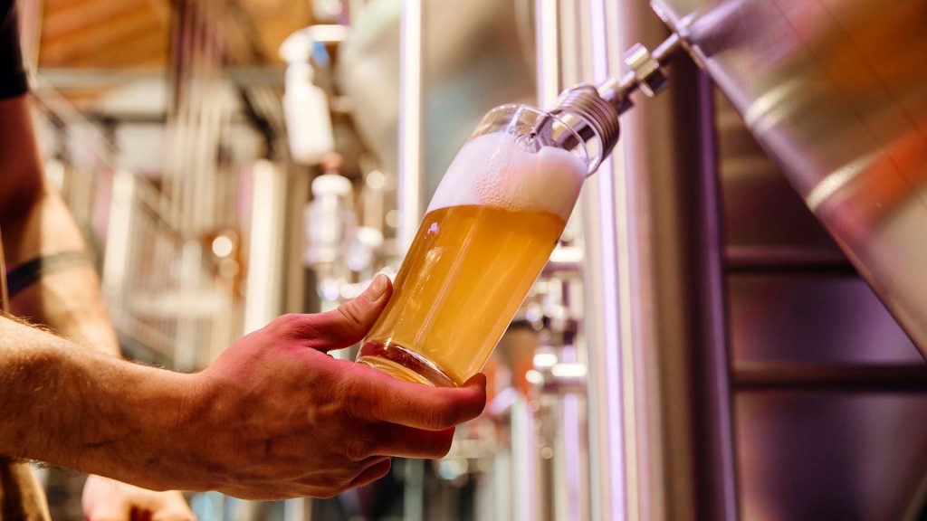 Zu sehen ist eine Hand, welche ein Glas hält, in welches Bier gezapft wird.