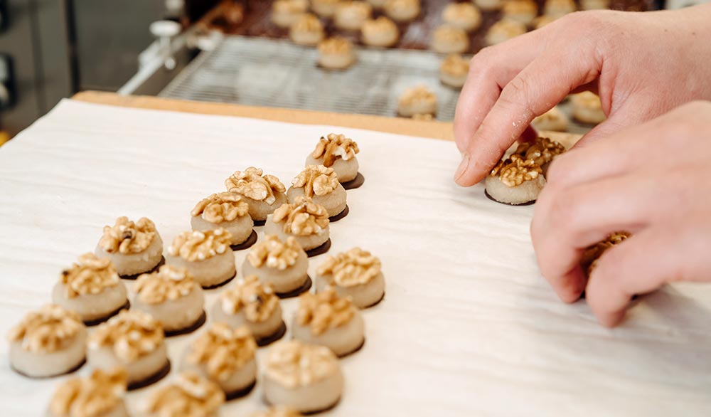 Man sieht zwei Hände, welche Pralinen anrichten, die mit Walnüssen verziert sind